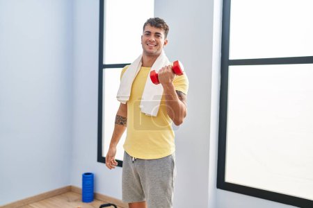 Photo for Young hispanic man smiling confident using dumbbell training at sport center - Royalty Free Image