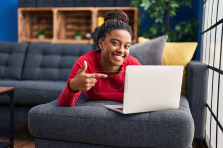 Téléchargez les photos : Jeune afro-américain avec des tresses fonctionnant à l'aide d'un ordinateur portable souriant heureux pointant avec la main et le doigt - en image libre de droit