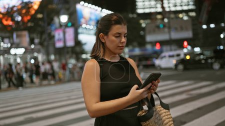 Photo for Beautiful hispanic woman engrossed in a serious phone conversation, using her smartphone on tokyo's vibrant streets under the city's night lights - Royalty Free Image