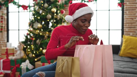 Foto de Mujer afroamericana celebrando la Navidad buscando bolsas de compras en casa - Imagen libre de derechos