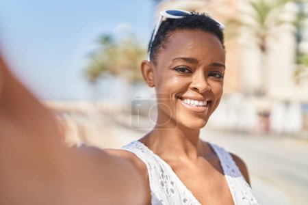 Téléchargez les photos : Afro-américaine femme souriant confiant faire selfie par caméra au bord de la mer - en image libre de droit