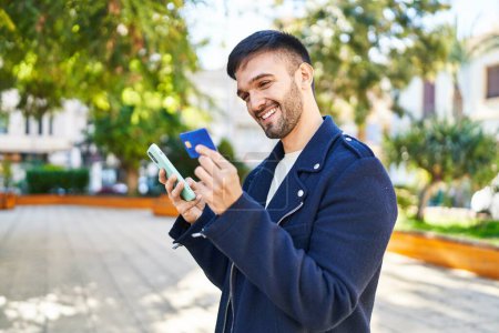 Téléchargez les photos : Jeune homme hispanique utilisant smartphone et carte de crédit au parc - en image libre de droit