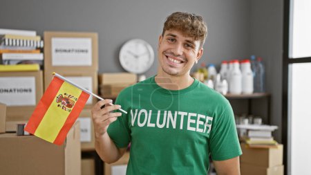 Photo for Portrait of a handsome, smiling young hispanic volunteer brimming with patriotism and altruism, holding the german flag at a busy charity center - Royalty Free Image