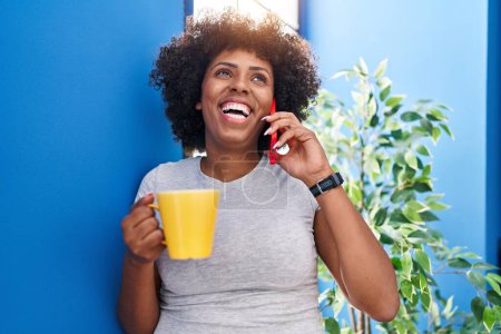 Foto de Mujer afroamericana hablando en smartphone bebiendo café en casa - Imagen libre de derechos