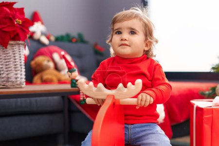 Photo for Adorable hispanic toddler playing with reindeer rocking by christmas tree at home - Royalty Free Image