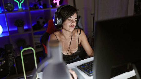 Foto de Mujer hispana joven perturbada streamer, hermoso jugador jugando videojuego en la computadora en la sala de juegos oscura, relajante pero concentrado - Imagen libre de derechos