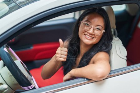 Photo for Young chinese woman driving car doing ok gesture with thumb up at street - Royalty Free Image