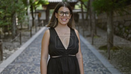 Téléchargez les photos : Joyeux et confiant, une belle femme hispanique dans des lunettes se tient près du temple ginkaku-ji serein, son sourire joyeux embrassant la beauté du jardin zen de kyoto - en image libre de droit
