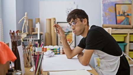 Photo for Captivating glimpse into a young hispanic man's world, artist, brush in hand, lost in thought while drawing at his studio - Royalty Free Image
