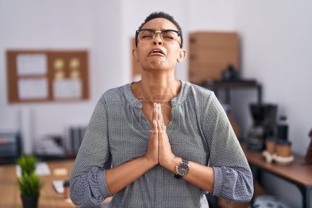 Téléchargez les photos : Femme afro-américaine travaillant au bureau portant des lunettes mendier et prier avec les mains ainsi que l'expression de l'espoir sur le visage très émotionnel et inquiet. mendier. - en image libre de droit