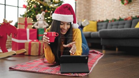 Téléchargez les photos : Jeune belle femme hispanique célébrant Noël boire du café regarder film sur touchpad à la maison - en image libre de droit