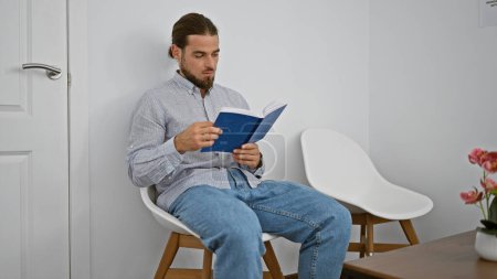 Téléchargez les photos : Jeune homme hispanique livre de lecture assis sur la chaise à la salle d'attente - en image libre de droit