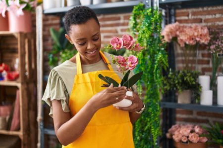 Téléchargez les photos : Afro-américaine femme fleuriste tenant plante chez le fleuriste - en image libre de droit