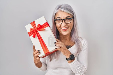 Foto de Mujer de mediana edad con el pelo gris sosteniendo regalo sonriendo y riendo en voz alta porque broma loca divertida. - Imagen libre de derechos