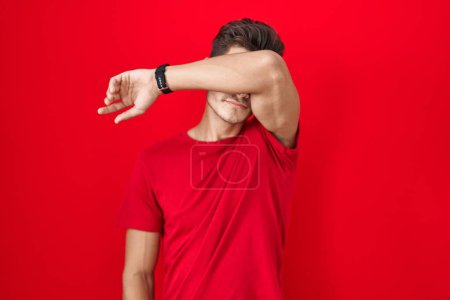 Photo for Young hispanic man standing over red background covering eyes with arm, looking serious and sad. sightless, hiding and rejection concept - Royalty Free Image