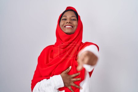 Téléchargez les photos : Jeune femme arabe portant une écharpe traditionnelle islamique en hijab se moquant de vous, pointant du doigt la caméra avec la main sur le corps, expression de honte - en image libre de droit
