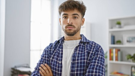 Photo for Serious young arab man stands with arms crossed in office, a successful professional worker exuding confidence in his business attire - Royalty Free Image