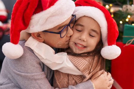 Photo for Brother and sister kissing and hugging each other sitting on floor by christmas gifts at home - Royalty Free Image