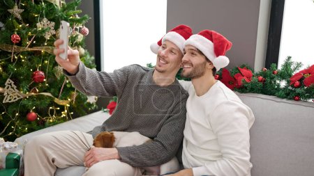 Foto de Dos hombres pareja celebrando la Navidad hacen selfie por teléfono inteligente en casa - Imagen libre de derechos