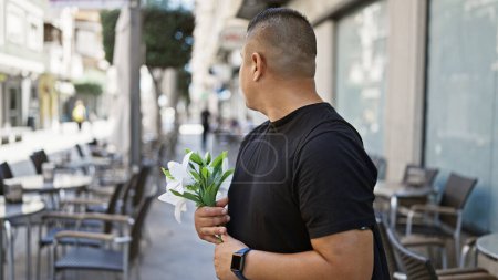 Foto de Hip, joven latino seriamente blandiendo un ramo de flores en una calle soleada de la ciudad, a la moda casual con un estilo de vida relajado - Imagen libre de derechos