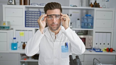 Foto de Joven científico hispano con gafas de seguridad y cara seria en el laboratorio - Imagen libre de derechos
