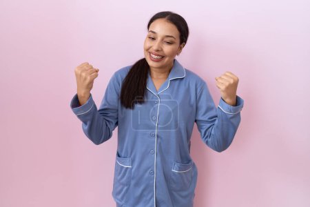 Téléchargez les photos : Jeune femme arabe portant un pyjama bleu très heureux et excité faisant geste gagnant avec les bras levés, souriant et criant pour le succès. concept de célébration. - en image libre de droit