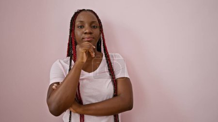 Photo for Beautiful african american adult woman rocks braids, pondering with doubt, a pipe dream over her mind, standing over an isolated pink wall background in deep thought, expression of disbelief - Royalty Free Image
