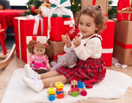 Photo for Adorable hispanic toddler holding star decoration sitting on floor by christmas gifts at home - Royalty Free Image