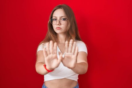 Photo for Young caucasian woman standing over red background moving away hands palms showing refusal and denial with afraid and disgusting expression. stop and forbidden. - Royalty Free Image