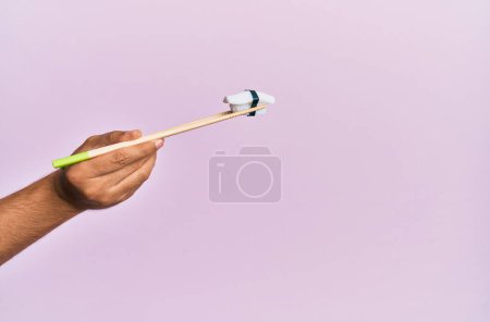 Téléchargez les photos : Main de l'homme tenant nigiri basse avec baguettes sur fond rose isolé - en image libre de droit