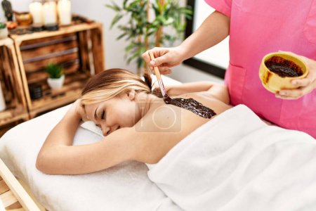 Photo for Young caucasian woman lying on table having back chocolate treatment at beauty salon - Royalty Free Image