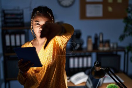 Téléchargez les photos : Femme afro-américaine avec des tresses travaillant au bureau la nuit avec la tablette regardant malheureux et en colère montrant rejet et négatif avec les pouces vers le bas geste. mauvaise expression. - en image libre de droit