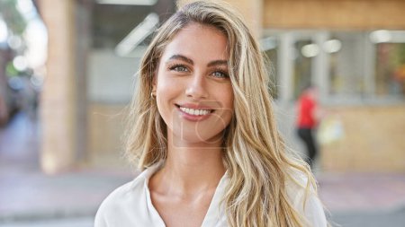 Photo for Radiant young blonde woman, exuding confidence with a sparkling smile, stands outdoors on a sunny city street, enjoying the urban ambiance and spreading positive vibes. - Royalty Free Image