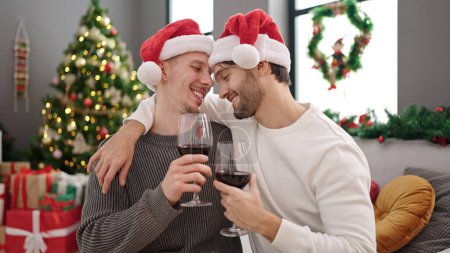 Téléchargez les photos : Deux hommes couple célébrant Noël boire du vin à la maison - en image libre de droit