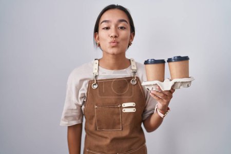 Photo for Young hispanic woman wearing professional waitress apron holding coffee looking at the camera blowing a kiss on air being lovely and sexy. love expression. - Royalty Free Image