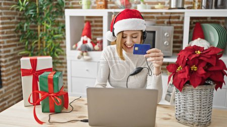 Téléchargez les photos : Jeune femme blonde faisant du shopping avec ordinateur portable et carte de crédit célébrant Noël dansant dans la salle à manger - en image libre de droit
