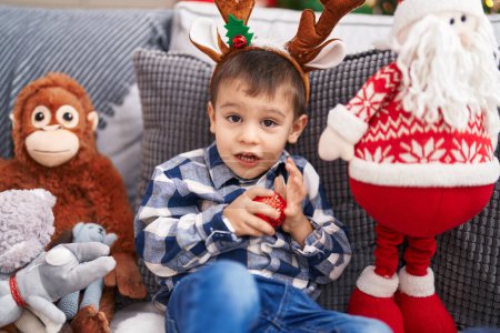 Téléchargez les photos : Adorable bambin portant des oreilles de renne assis sur le canapé près de l'arbre de Noël à la maison - en image libre de droit