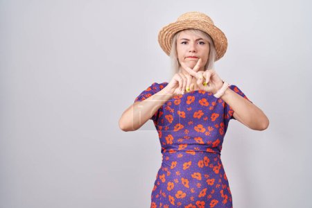 Téléchargez les photos : Jeune femme caucasienne portant des fleurs robe et chapeau d'été rejet expression croisement doigts faire signe négatif - en image libre de droit