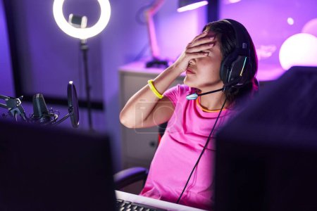 Foto de Young hispanic woman streamer stressed using computer at gaming room - Imagen libre de derechos