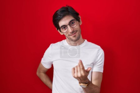 Téléchargez les photos : Jeune homme hispanique debout sur fond rouge signe venir ici geste avec la main invitant accueillant heureux et souriant - en image libre de droit