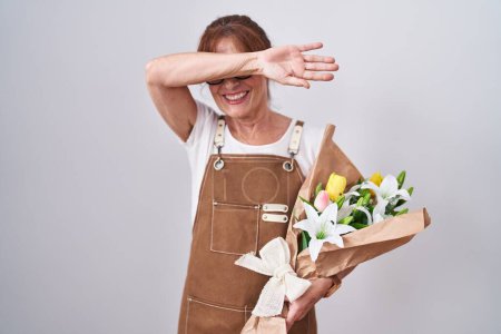 Foto de Mujer de mediana edad sosteniendo ramo de flores blancas sonriendo alegre jugando a echar un vistazo a un boo con las manos mostrando la cara. sorprendido y salido - Imagen libre de derechos