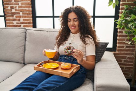 Photo for Young beautiful hispanic woman having breakfast sitting on sofa at home - Royalty Free Image