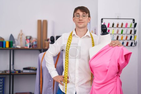 Téléchargez les photos : Jeune homme caucasien tailleur souriant confiant étreignant mannequin au magasin de tailleur - en image libre de droit