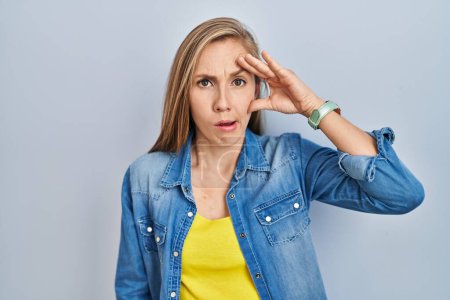 Photo for Young blonde woman standing over blue background worried and stressed about a problem with hand on forehead, nervous and anxious for crisis - Royalty Free Image