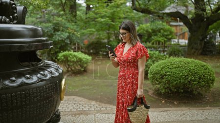 Photo for Hispanic woman in glasses captures japan's ancient gotokuji temple beauty with her phone, enjoying her role as a tourist - Royalty Free Image
