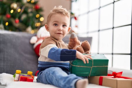 Photo for Adorable toddler unpacking christmas gift sitting on sofa at home - Royalty Free Image