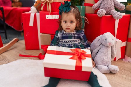 Foto de Adorable rubia niño desempacar regalo sentado junto al árbol de Navidad en casa - Imagen libre de derechos
