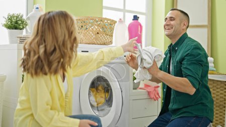 Téléchargez les photos : Homme et femme couple lavage vêtements ensemble sourire à buanderie - en image libre de droit