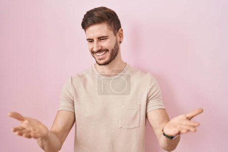 Foto de Hombre hispano con barba de pie sobre fondo rosa sonriente alegre con los brazos abiertos como bienvenida amistosa, saludos positivos y confiados - Imagen libre de derechos