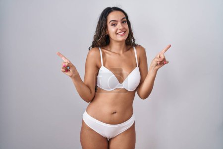 Téléchargez les photos : Jeune femme hispanique portant de la lingerie blanche souriant confiant pointant avec les doigts vers différentes directions. espace de copie pour la publicité - en image libre de droit